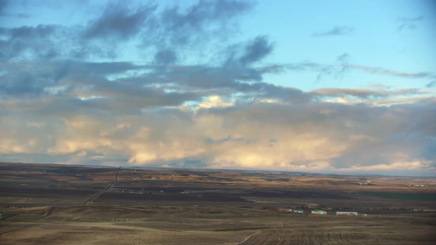 Looking over an expansive rural agricultural valley in Autumn with sunset clouds hanging heavy under a blue sky and farmhouses dotting the horizon