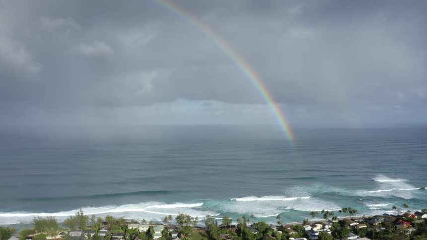 Rainbow over ocean along the coast lined with houses and trees