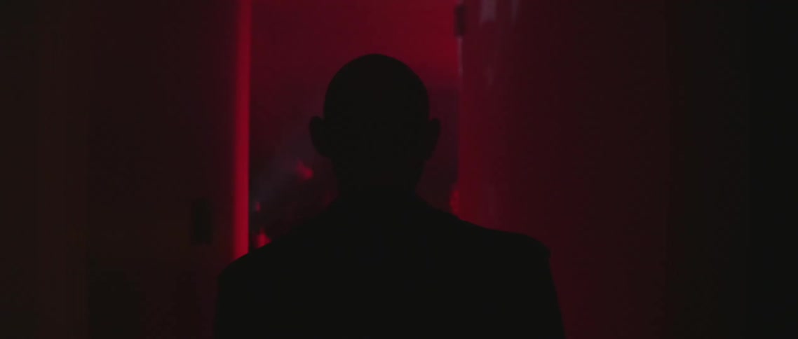 A silhouette of a person standing in a hallway with red flashing lights