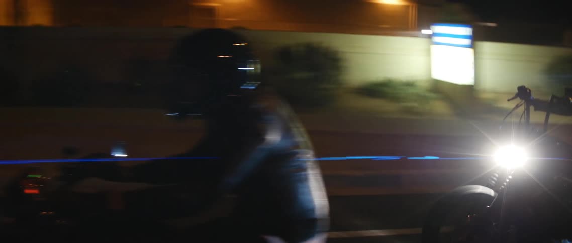 Two people wearing crash helmets and leather jackets riding motorcycles at night in the city