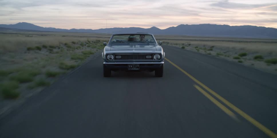 A woman leans over to give her boyfriend a kiss on the cheek as they speed down a rural highway in a vintage car