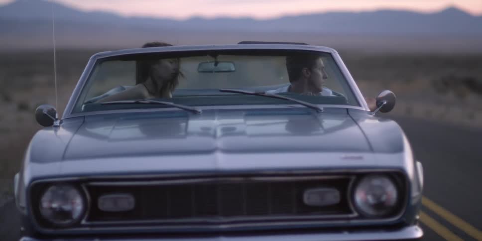 Young couple driving a convertible car on a road through the desert at sunset