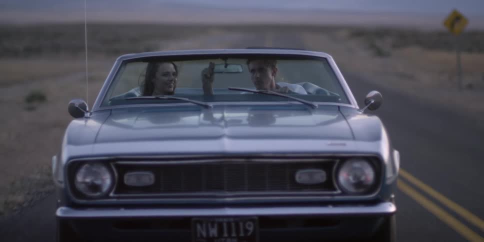 A man adjusts his rearview mirror while driving with his girlfriend down a rural road