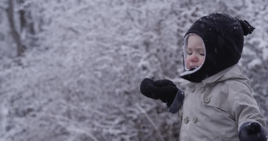 A bundled up toddler walks outside while snow is falling