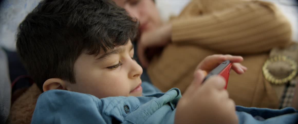 A child lays on the bed using his phone