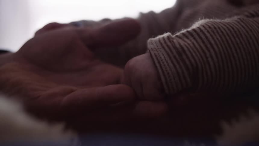 A man puts his hand under his babys hands and caresses him
