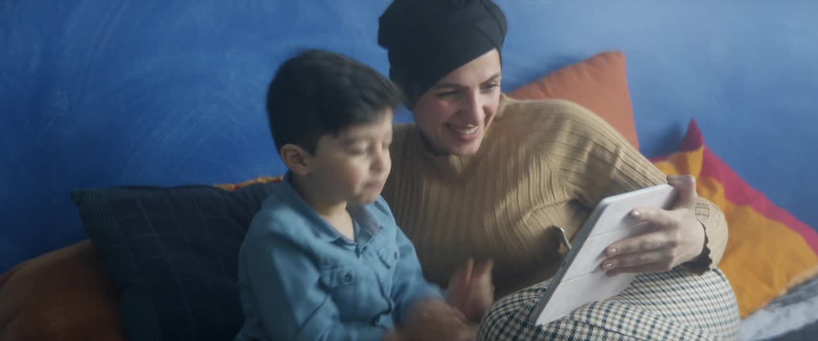 A mother and her son wave at people on a tablet