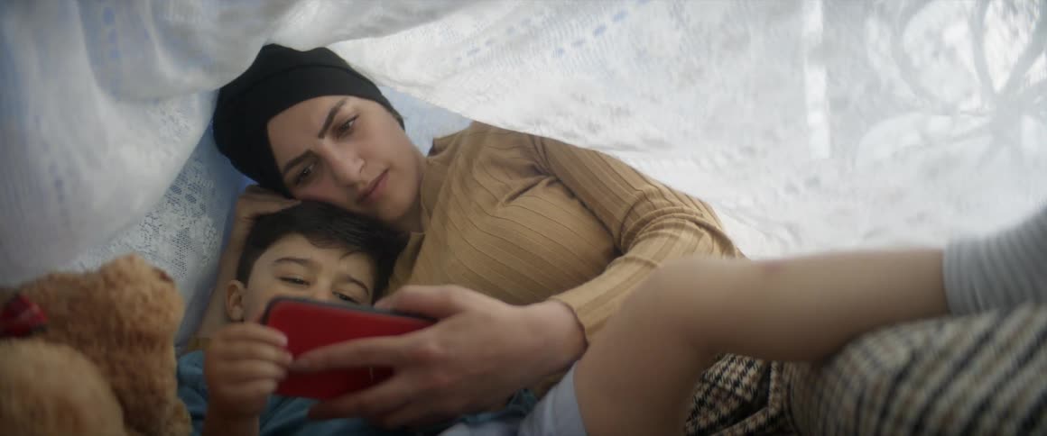 Mother and son using a smart phone while relaxing in bed at home