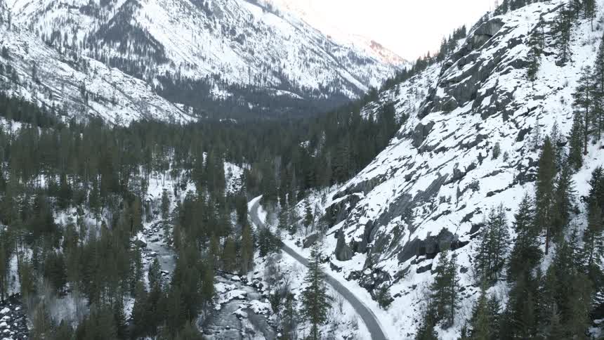 An empty road winds through a snowy mountain valley