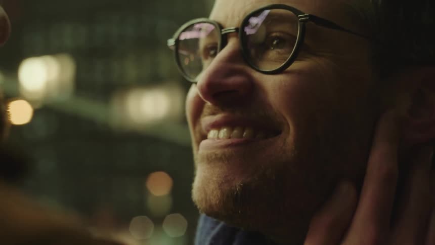A man smiles and gazes at his boyfriend as his face is caressed and they kiss