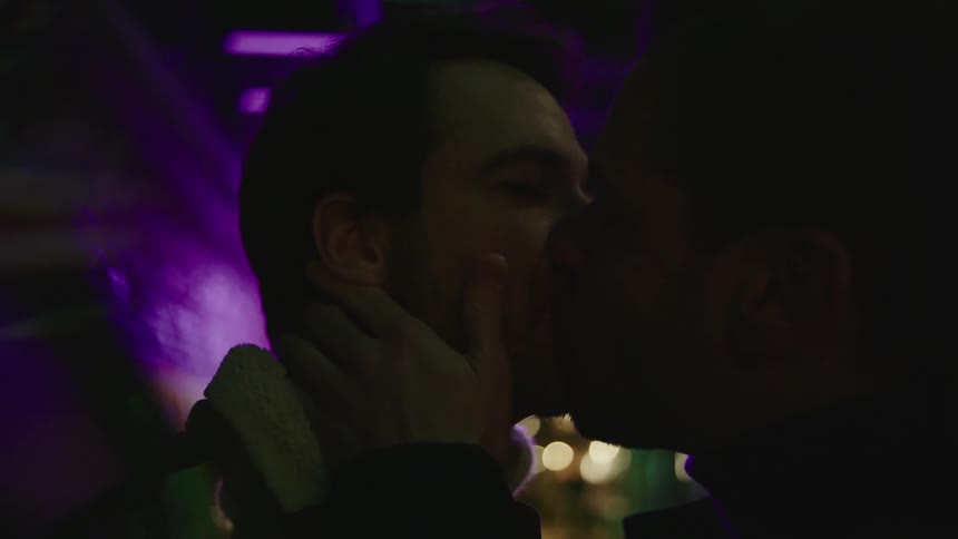 Two men smiling and kissing in the dark