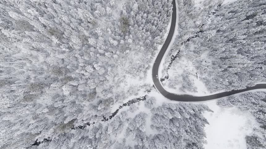 A car travels on a curvy mountain road through a snow covered winter wonderland