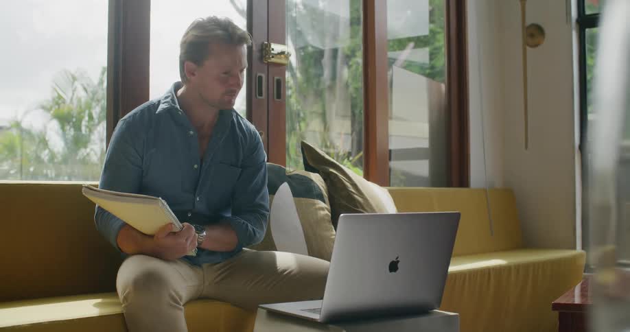 A man is sitting indoors and looking at a laptop