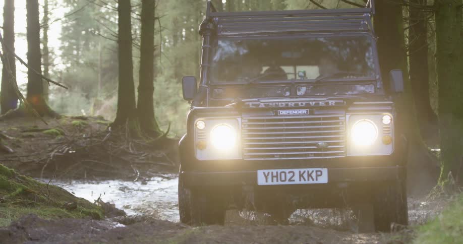 A vehicle driving in a forest with trees with water and mud