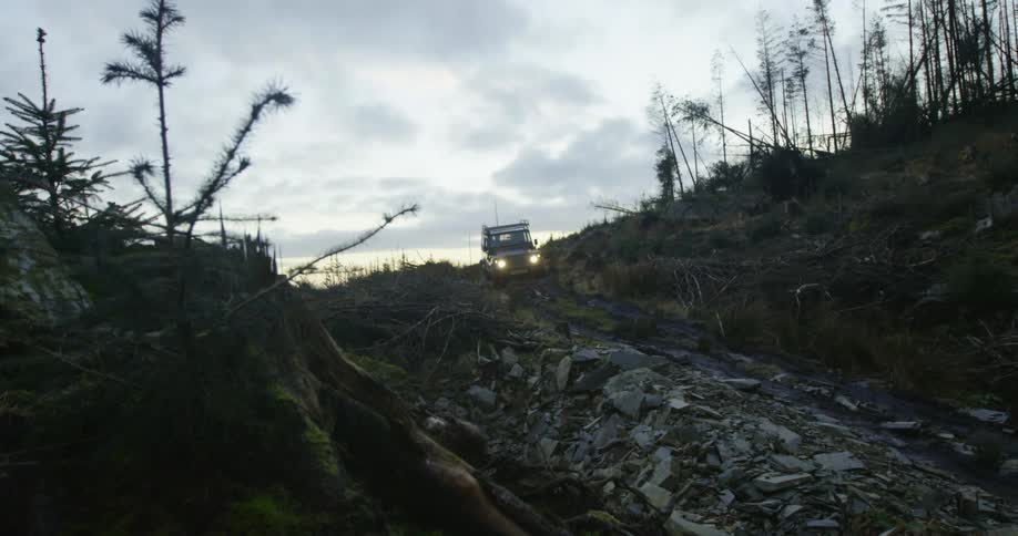 A vehicle driving on a rocky road surrounded by trees and grass