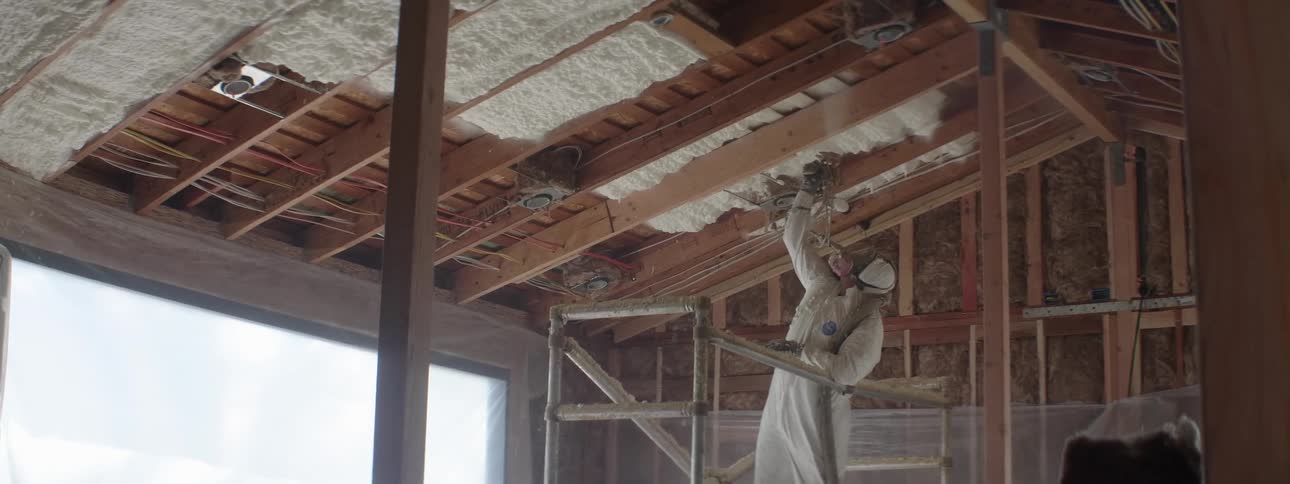 A construction worker spraying insulation onto the ceiling of a new building