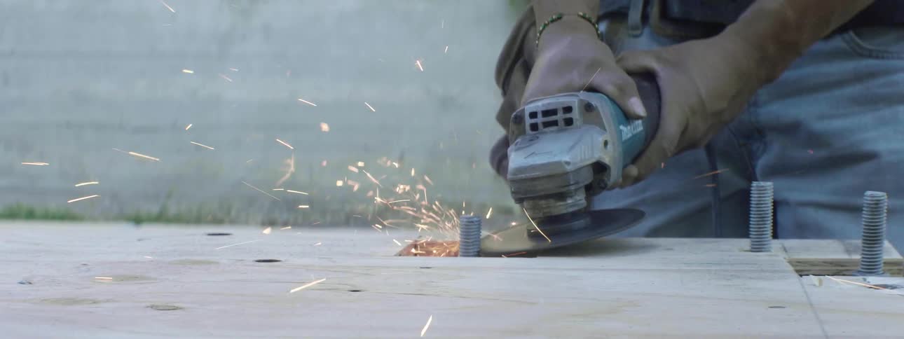 A construction worker is using a angle grinder to cut bolts