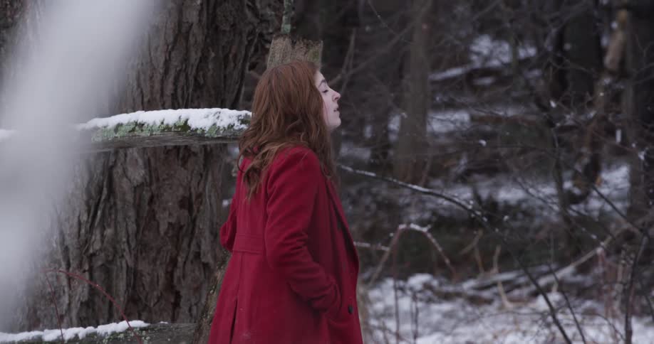 A woman wearing a coat stands in a wooded area and smiles