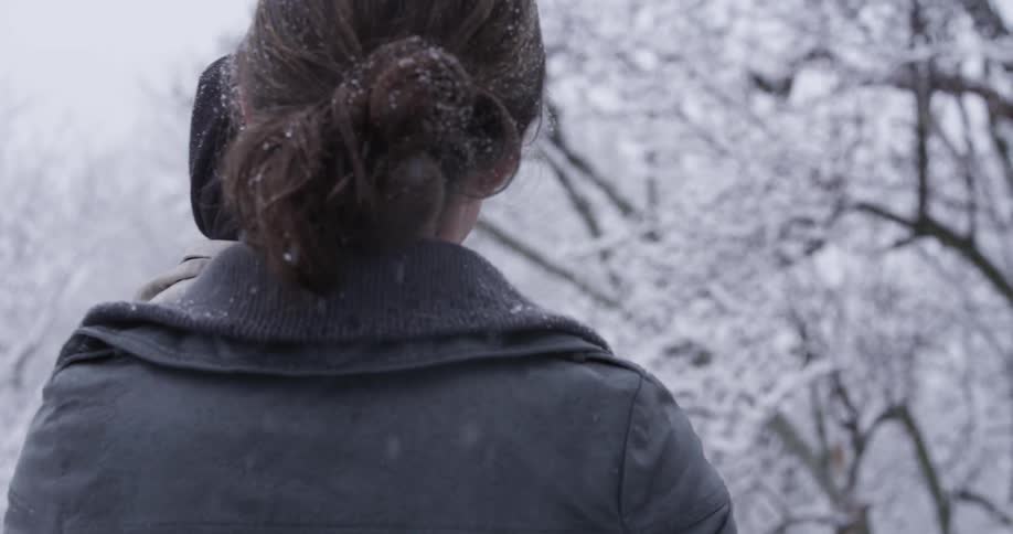 A woman is holding a baby as it snows around them
