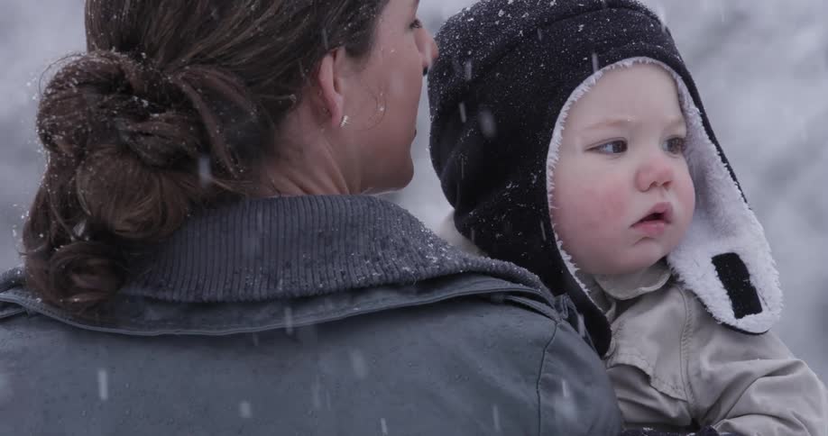 A woman has a baby in her arms as it snows