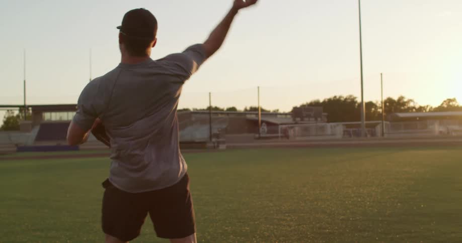 A man in a baseball field catching and throwing a baseball with the sky and clouds in the background