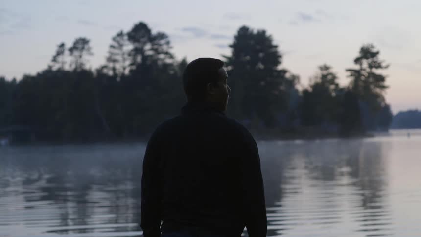 A man stands before a lake at sunset