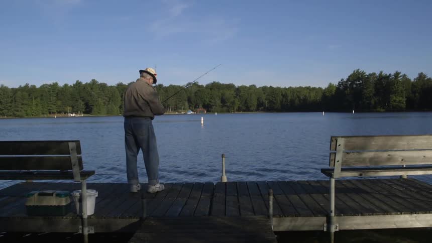 An older man stands on a pier adjusting a fishing rod