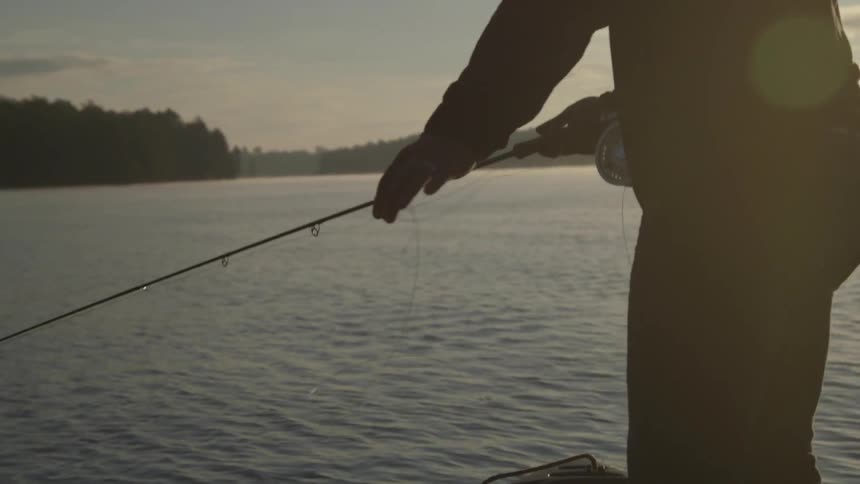 A man fishes off a boat at sunrise