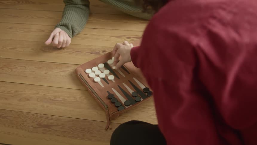 Pair of people play backgammon sitting on wooden floor