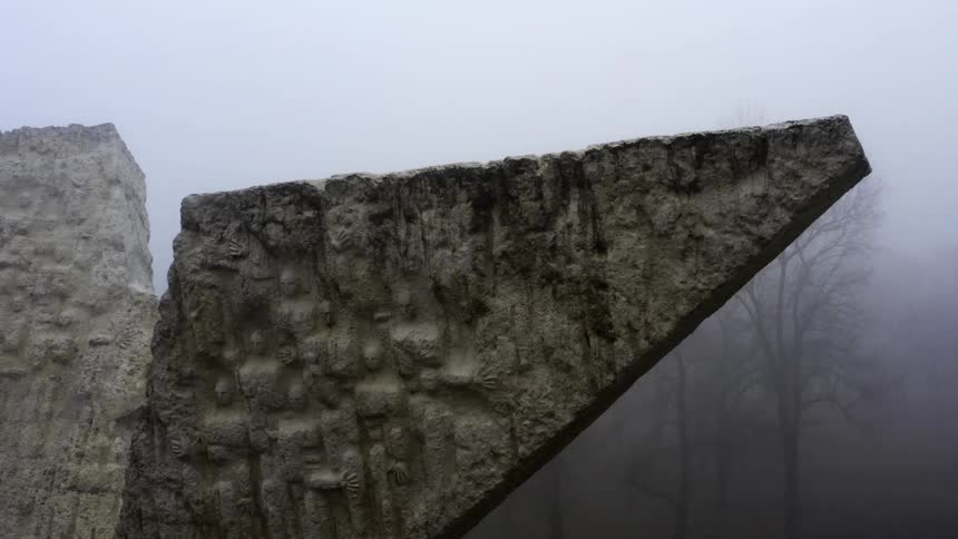 Large stone wedges with faces carved into them stand with trees and fog behind