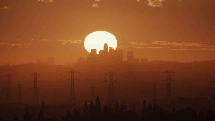 Silhouettes of utility towers and buildings as the sun sets in an orange sky
