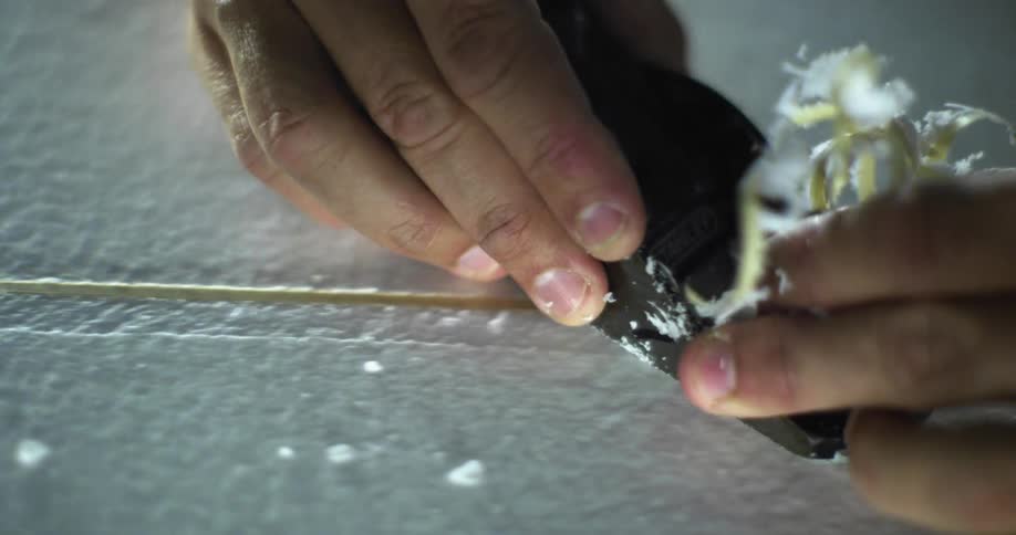 A man shaves wood as he makes a surfboard
