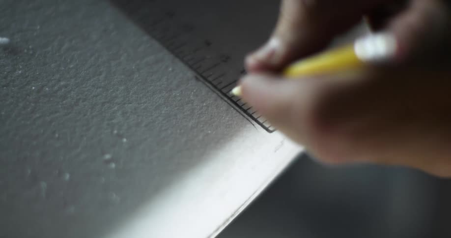 A man draws a line against a ruler with a pencil