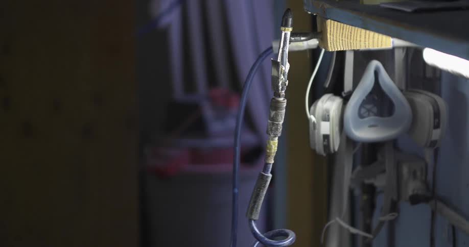 A hand covered in white paint reaches over and hooks a cord and a hook to a clip on the side of a machine
