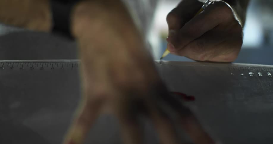 A person with a pencil and a ruler making marks on a surfboard