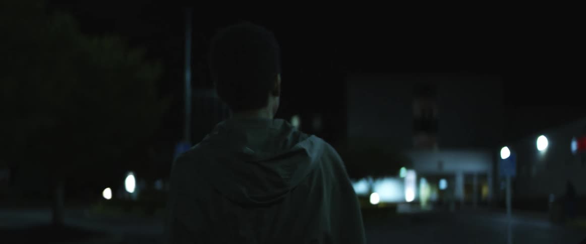 A male walking alone on a city sidewalk at night