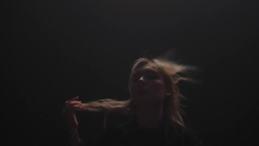 A woman with a jacket walking on a stage with a flashing screen behind her