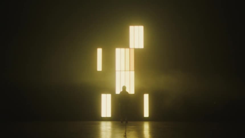 Silhouette of a woman modeling in front of a big screen projected on the wall of a smoky dark room