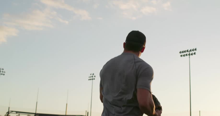 A strong man catching a baseball in a stadium at sunset