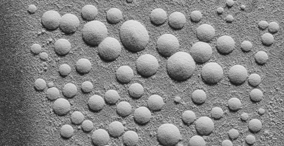 Drops of water covered in white dust move and shatter over a vibrating surface