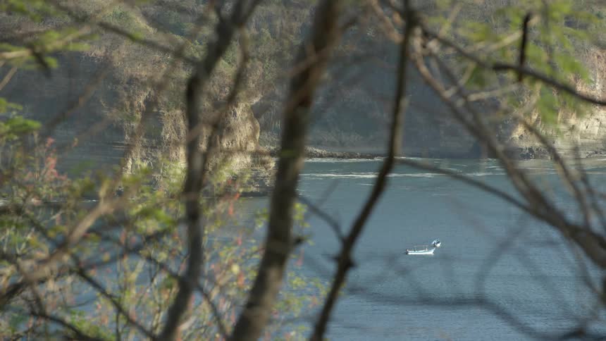 A small white boat sits alone in a large lake near a canyon
