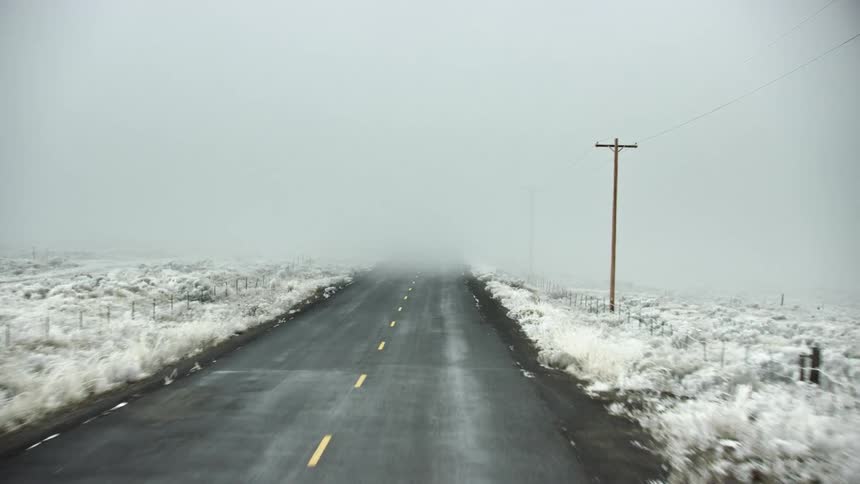 Looking forward driving down a foggy and snowy rural road on the way to Thanksgiving dinner with telephone poles and snow covering the dry meadow and sagebrush