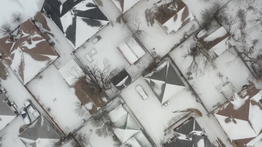 Aerial of snow falling on a snow covered neighborhood