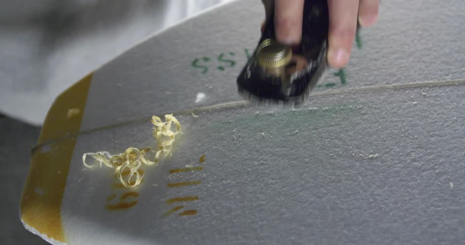 A man sanding down a surfboard in a shop