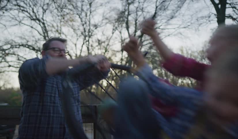 A father pushes his two daughters on a circle flat swing outdoors in a park at sunset
