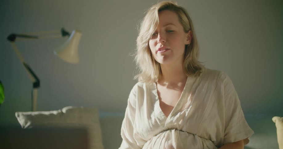 Young pregnant woman wearing a white dress talking on a video call through a laptop