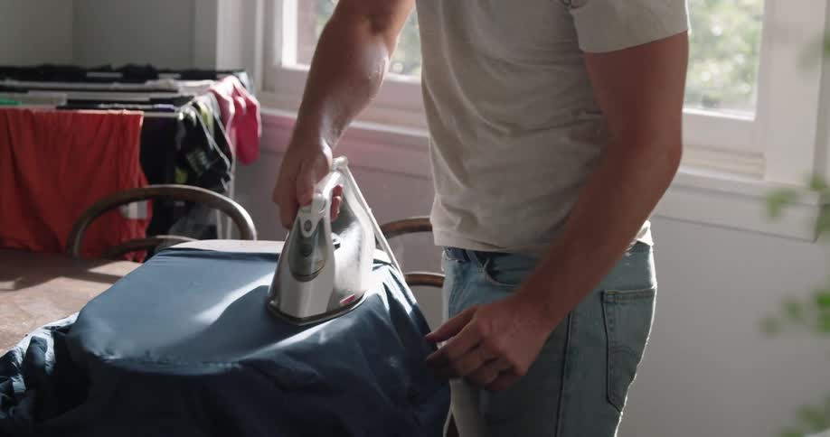 Blonde man with white shirt and jeans does the ironing in the room