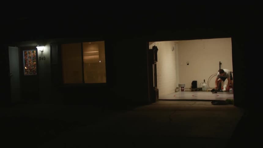 A boy in an open garage at nighttime practicing wresting moves