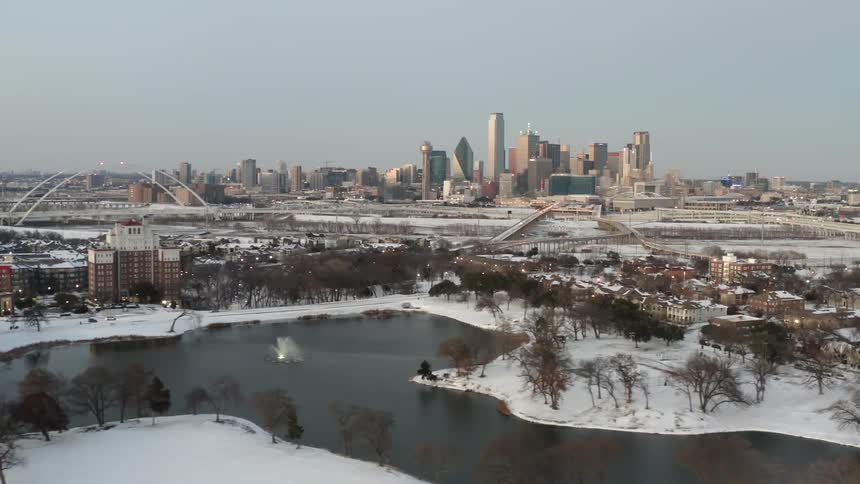 An aerial view of a neighborhood with snow next to a small lake with a distant view of high rise buildings on the horizon