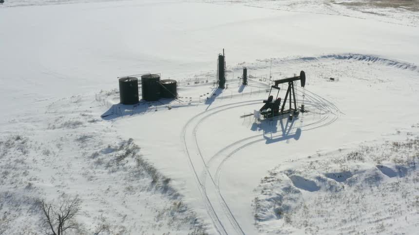 Aerial view of a single oil pump working on an oilfield covered in snow at winter